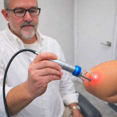 Chiropractor applying high-intensity Class IV laser therapy to a patient's elbow at Hanson Chiropractic Center in Edmond.